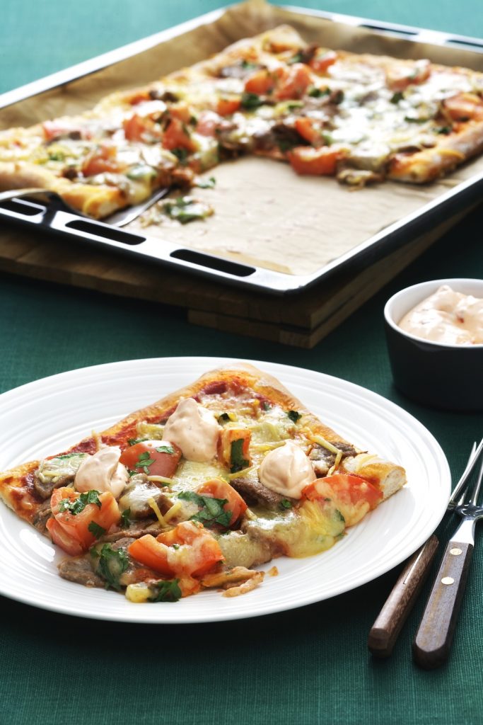 Kebabpizza med färska tomater och persilja upplagt på en vit tallrik