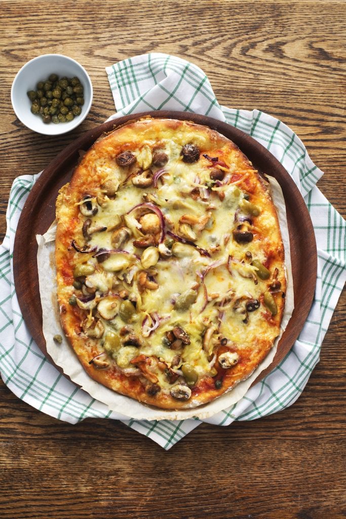 Pizza med blandsvamp, vitlök, kapris och oliver på kökshandduk