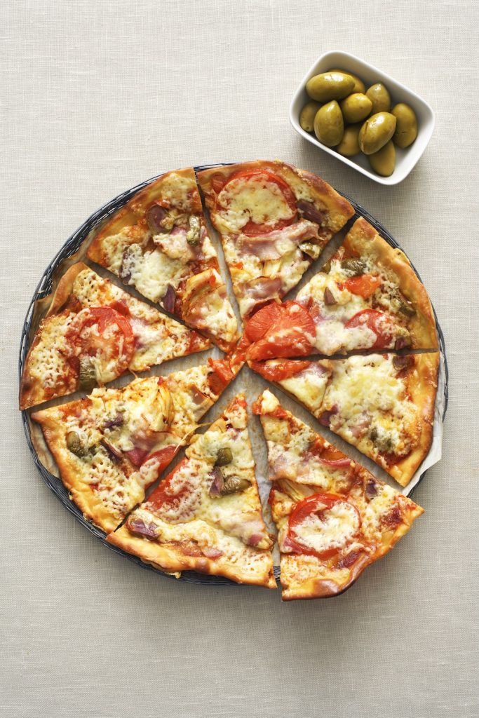 Pizza uppdelad i slizes, med tomat, gröna oliver, bacon och kyckling