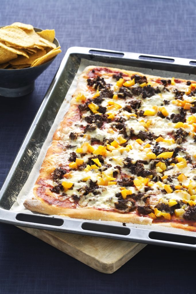 Tacopizza på plåt med tortillachips i bakgrunden