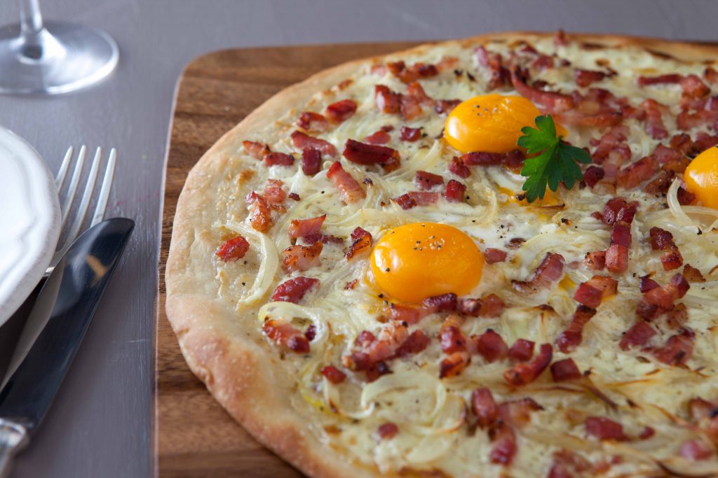 Klassisk pizza med ägg, bacon och lök på en träskärbräda.
