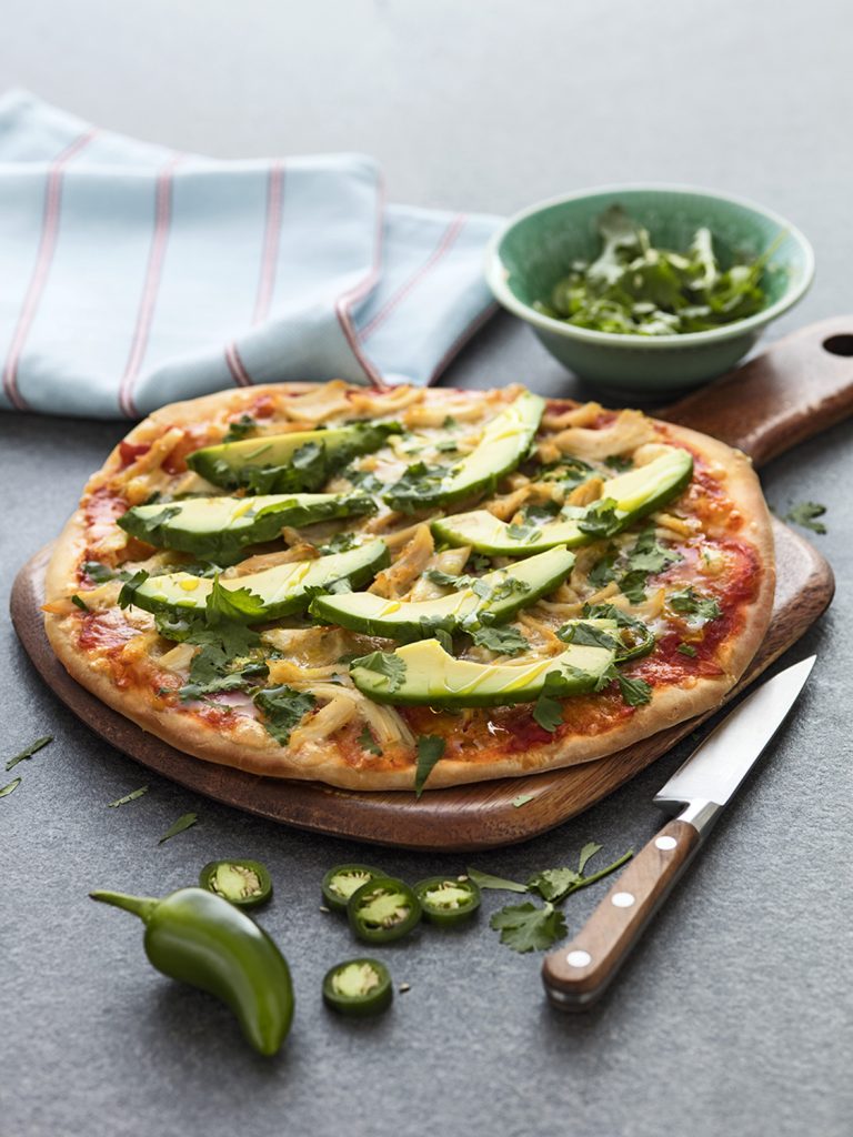 Färsk vegansk pizza med avokado, jalapeños och koriander på ett träbräda.