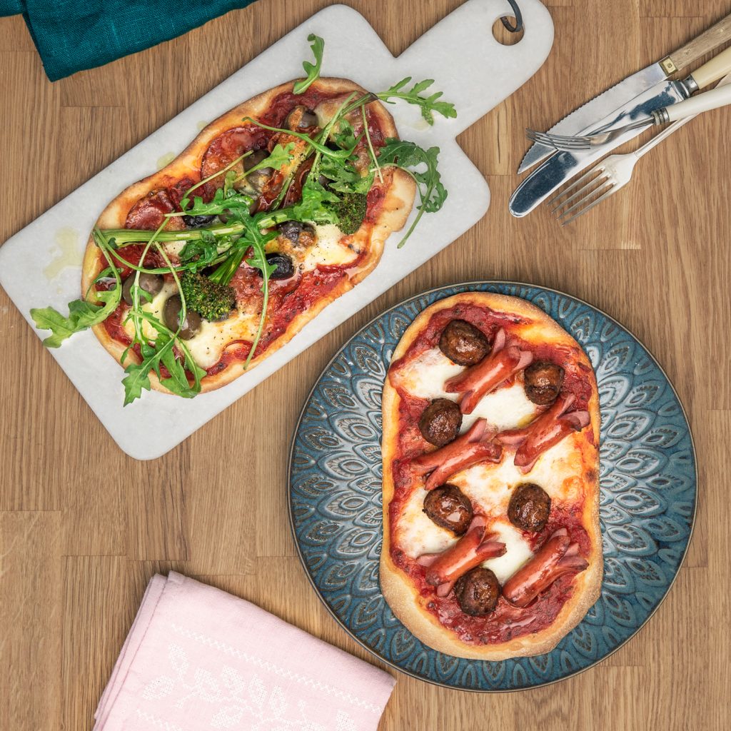 Färska pizzor med köttbullar, skinka och grönt på stenplatta och talrikt, rustikt bord.