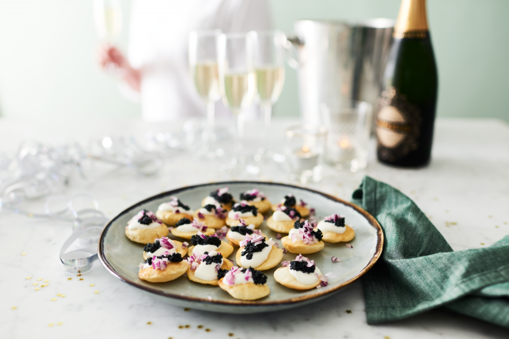 Kaviarpuffar på ett fat med champagneglas i bakgrunden. Festkänsla.