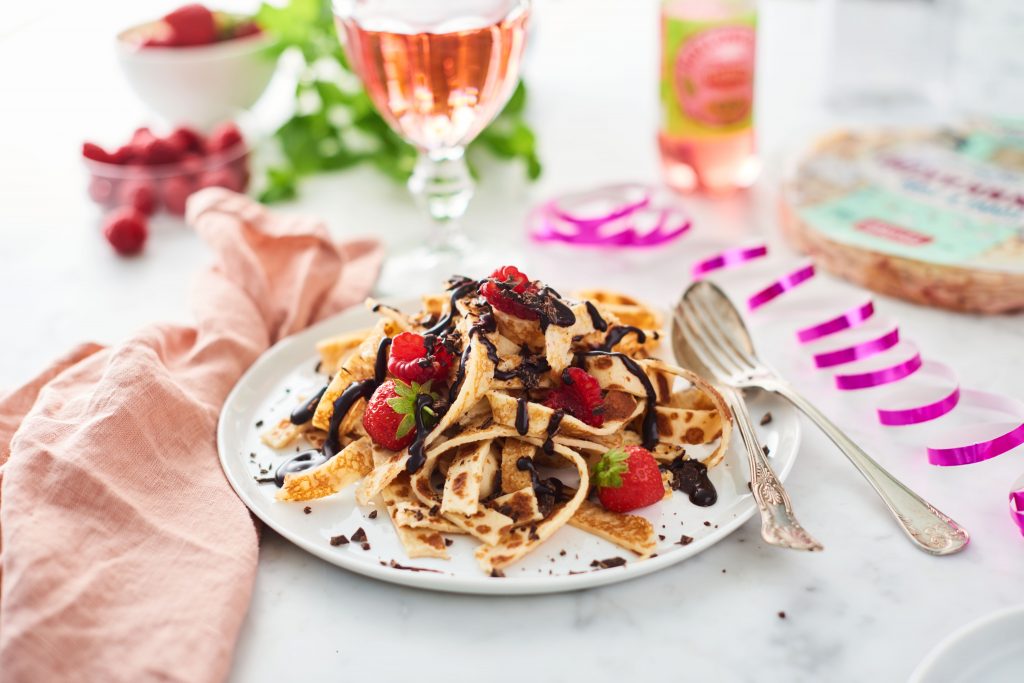 Strimlad pannkaka på en tallrik. Med färska bär och smält choklad.