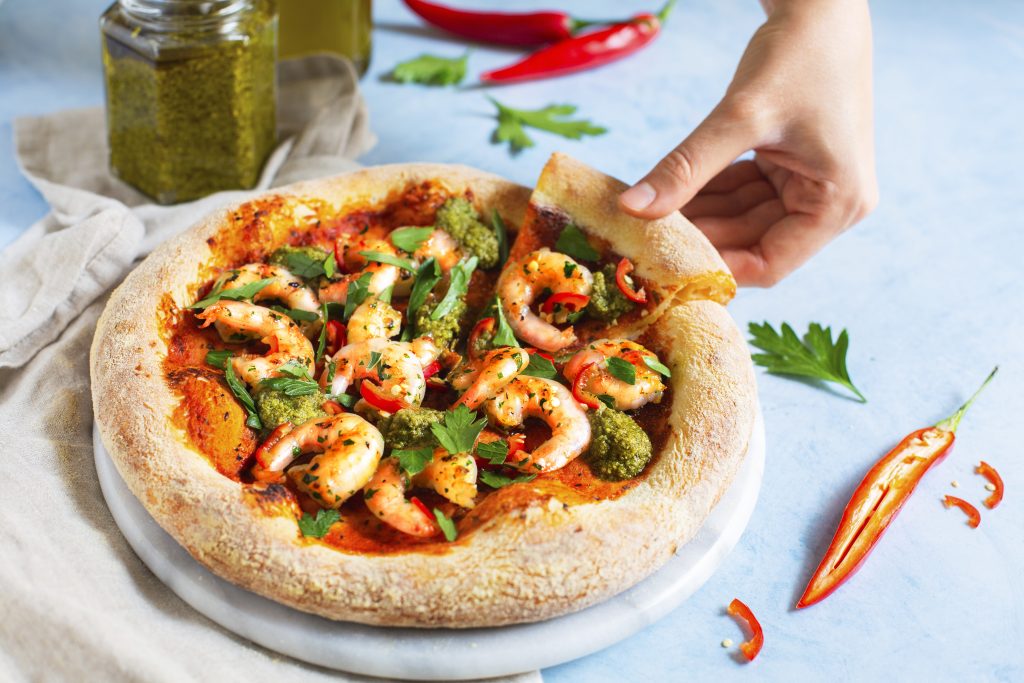 En rund pizza med j&auml;tter&auml;kor. En hand tar en bit av den goda pizzan.